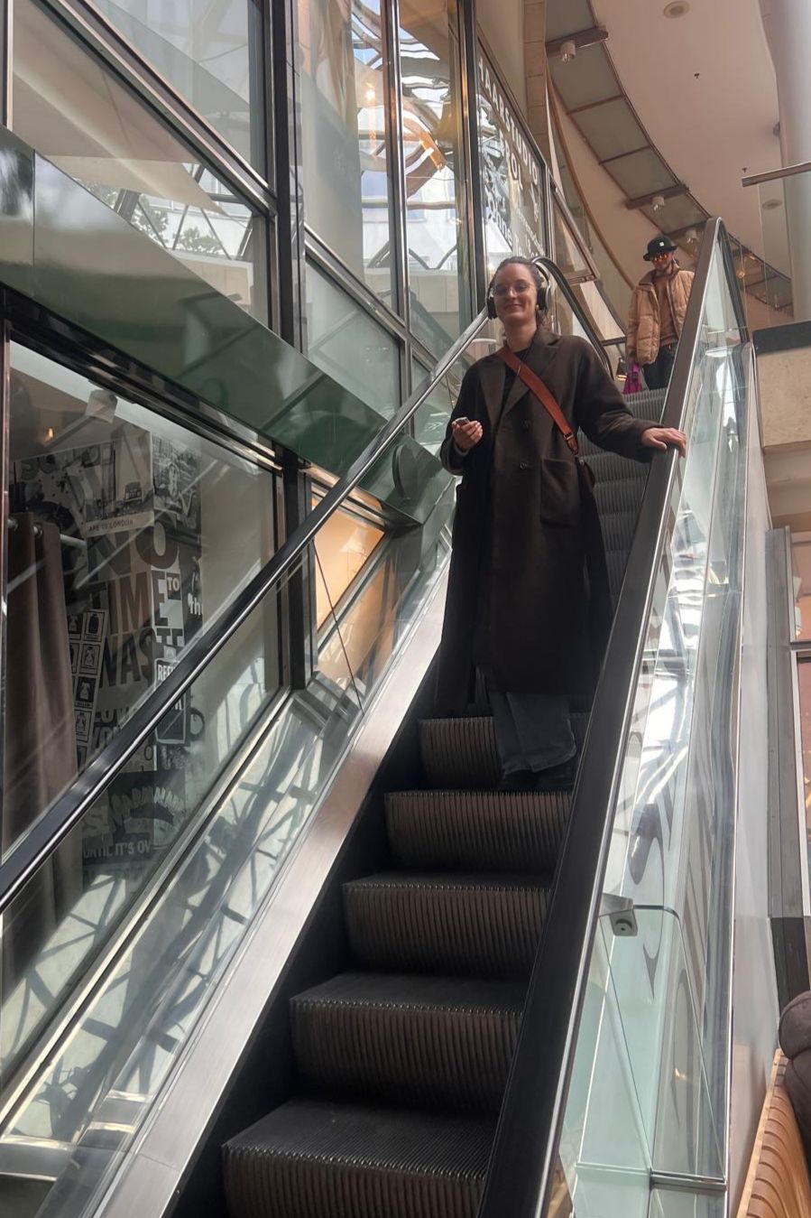 Eine Frau mit Kopfhörern fährt die Rolltreppe runter.